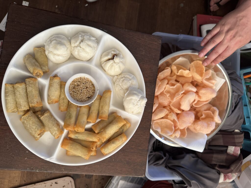 Photo of a white plate with spring rolls and steamed pork buns. Sitting next to that is a bowl of prawn crackers.